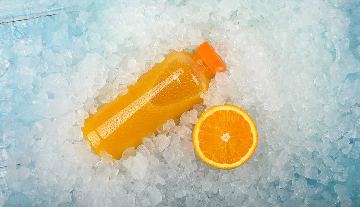 Close up one plastic PET bottle of fresh orange juice and cut half orange slice over background of crushed ice, elevated high angle view, directly above