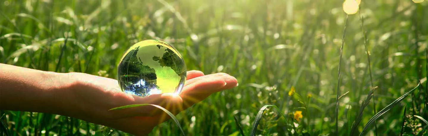 Earth crystal glass globe in human hand on grass background